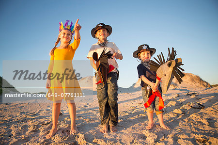Sister and brothers dressed as native american and cowboys pointing from sand dunes