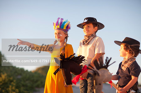 Three children dressed as native american and cowboys pointing from sand dunes