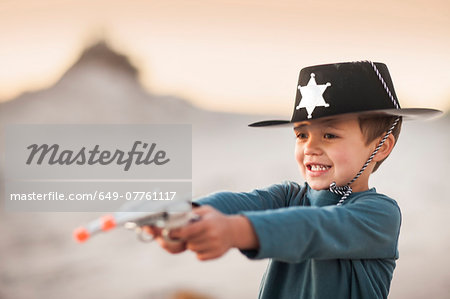 Boy dressed as cowboy sheriff holding pointing toy guns in sand dunes