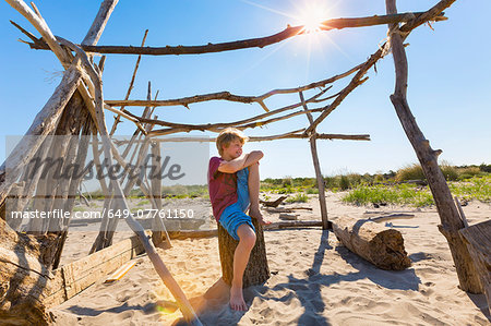 Boy making a break in driftwood shelter, Caleri Beach, Veneto, Italy