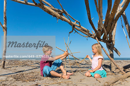 Boy and his sister constructing a circular structure from driftwood, Caleri Beach, Veneto, Italy