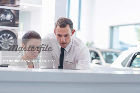 Salesman and saleswoman at desk in car dealership