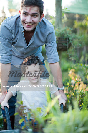 Portrait of  mid adult man and son pushing wheelbarrow in allotment