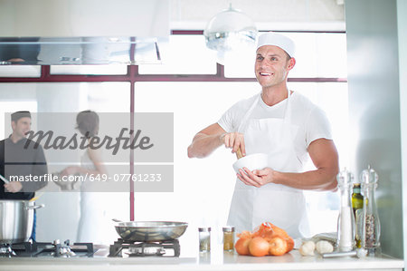Portrait of smiling male chef mixing with mortar and pestle in commercial kitchen