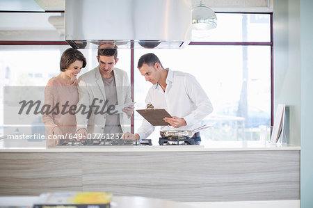 Mid adult couple and salesman looking at hob in kitchen showroom