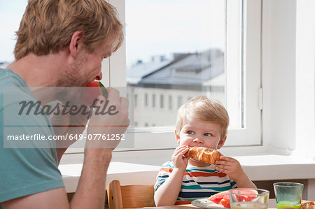 Father and toddler son eating breakfast at kitchen table