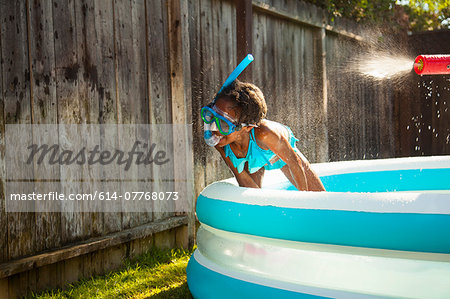 Girl in scuba mask getting sprayed with water gun in garden paddling pool