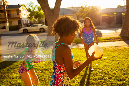 Three girls playing with water balloons in garden