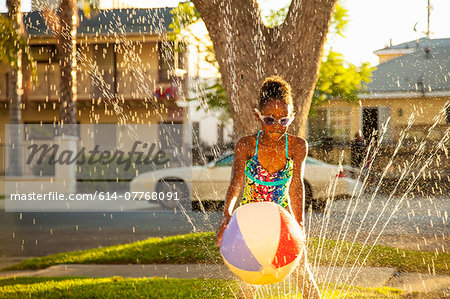 Girl with beachball in garden sprinkler