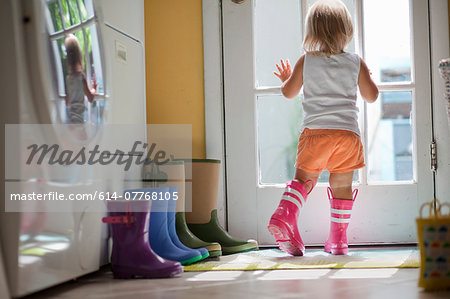 Female toddler wearing rubber boots looking out of back door window