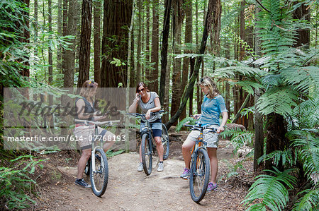 Three mid adult women mountain bikers using smartphones  in forest