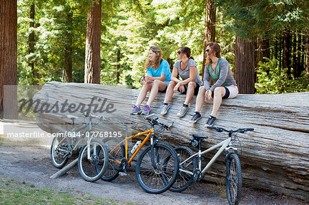 Three women mountain bikers sitting on tree trunk in forest