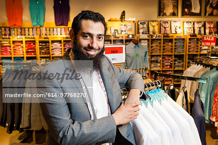 Portrait of tailor leaning against rails in men's clothes shop