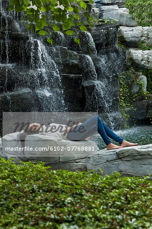 Young woman with headphones near waterfall, Thailand