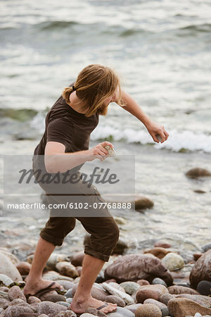 Young man throwing stones on beach, Gotland, Sweden