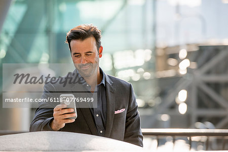 A man seated on a bench checking his smart phone.