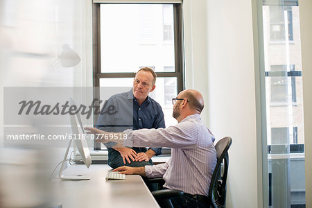 Two business colleagues in an office talking and referring to a computer screen.