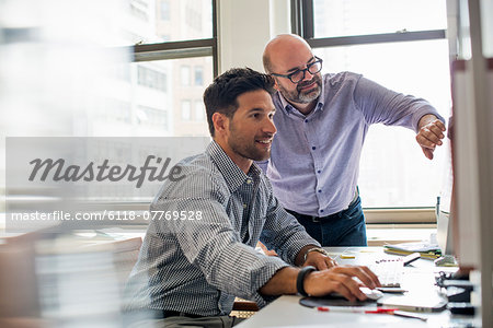 Office life. Two men in an office, using a computer screen.