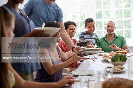 A family gathering, men, women and children around a dining table sharing a meal.