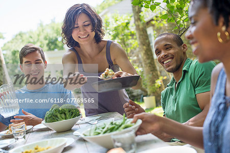 A family gathering, men, women and children around a table in a garden in summer.