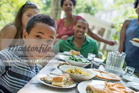 A family gathering, men, women and children around a table in a garden in summer. A boy smiling in the foreground.