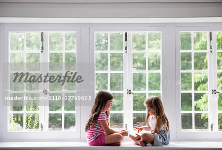 Two girls sitting indoors cross legged.