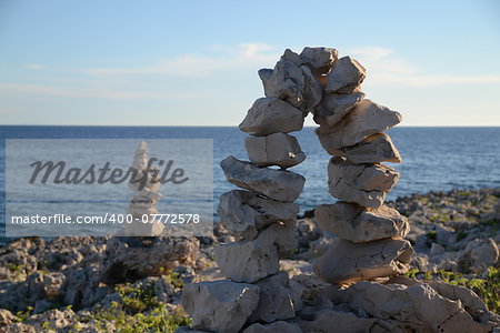 Pyramid of stones at the ocean. Blue water background in summertime.