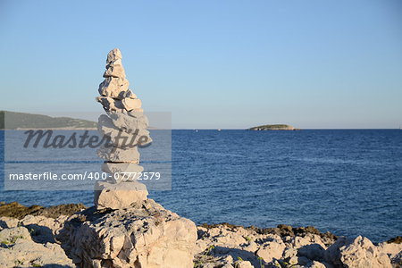 Pyramid of stones at the ocean. Blue water background in summertime.