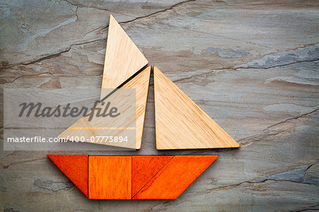 abstract picture of a sailing boat built from seven tangram wooden pieces over a slate rock background, travel or vacation concept, artwork created by the photographer