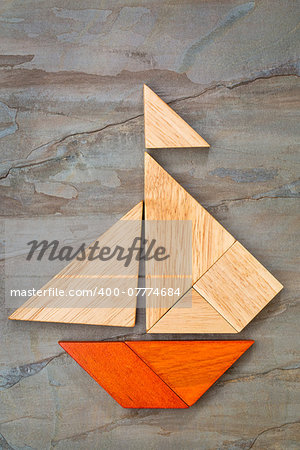 abstract picture of a sailing boat built from seven tangram wooden pieces over a slate rock background, artwork created by the photographer