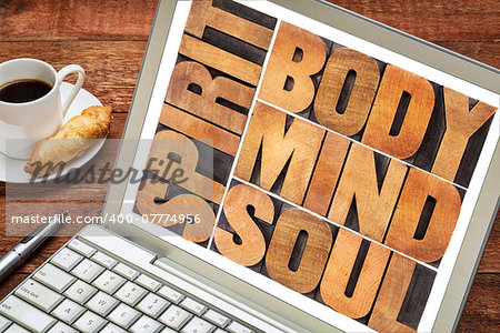 body, mind, soul and spirit word abstract - a collage of isolated text in vintage wood letterpress printing blocks on a laptop screen with a cup of coffee