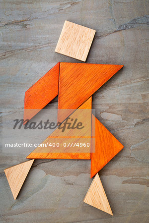 abstract of a dancing or walking figure built from seven tangram wooden pieces, a traditional Chinese puzzle game; slate rock background background, the artwork copyright by the photographer