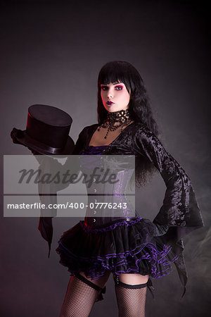 Magician assistant in purple and black gothic Halloween outfit, studio shot on black background