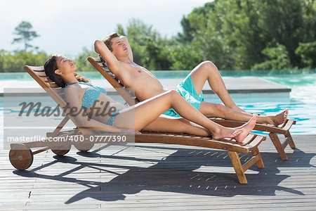 Full length of a young couple sitting on sun loungers by swimming pool