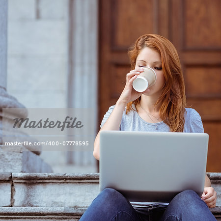 Beautiful woman drinking of disposable cup using her laptop in the street