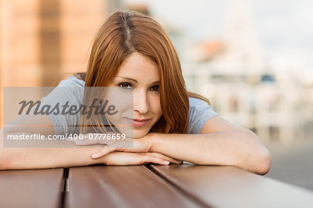 Smiling pretty redhead lying on bench on a sunny day in the city