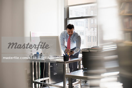 A man standing at his desk using his phone, dialling or texting.