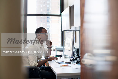 A man working in an office seated at a desk. Looking at a computer screen.