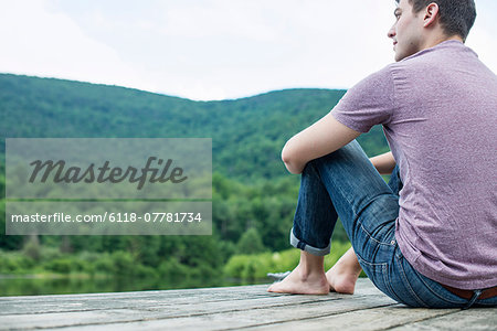 A man sitting on a wooden pier by a lake in summer A man sitting on a wooden pier by a lake in summer