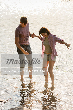 A couple holding hands, paddling in shallow water at the lake.