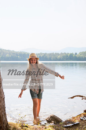 A girl in a straw hat paddling in the shallow waters of a mountain lake.