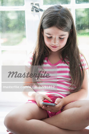 A girl sitting playing, holding a smart phone.