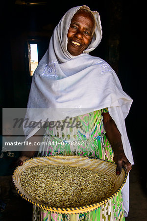 Friendly old woman standing with a basket of corn in a door frame, near Keren, Eritrea, Africa