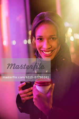 Woman on city street with coffee and cell phone at night