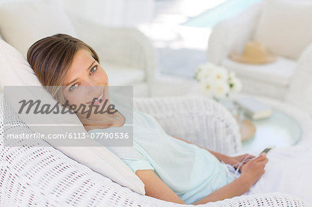 Smiling woman using cell phone in wicker chair