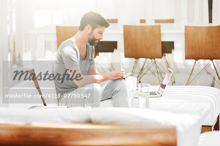 Man writing notes at laptop on sofa in modern living room