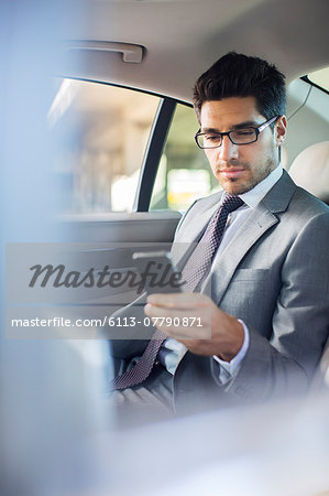 Businessman using cell phone in car back seat