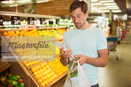 Surprised man reading receipt in grocery store