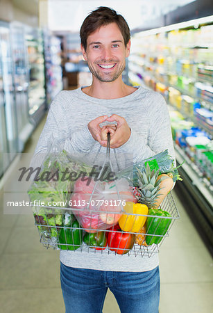 Man holding full shopping basket in grocery store