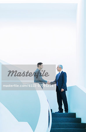 Businessmen shaking hands on stairs of office building